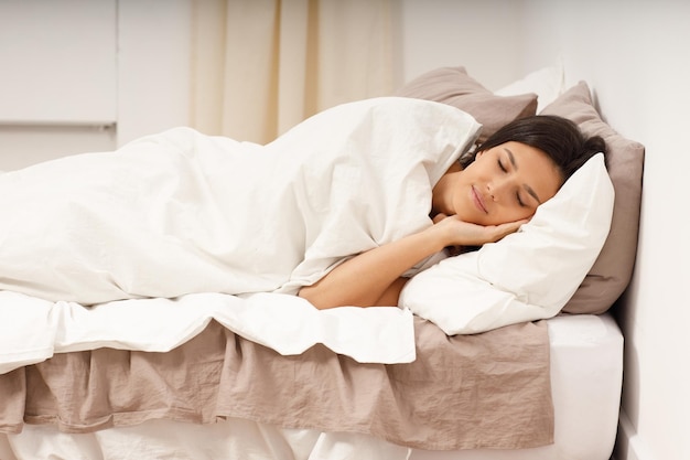 Une jeune femme en bonne santé couvre une couverture qui dort les yeux fermés sur le lit dans la chambre