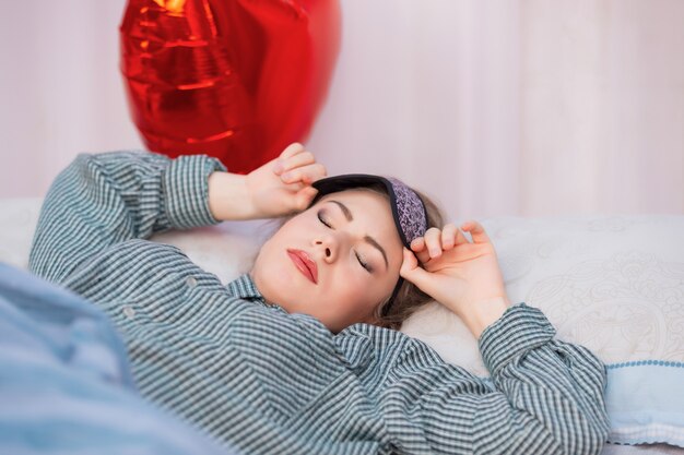 Une jeune femme en bonne santé en pyjama se réveille de son sommeil, enlève son masque de sommeil