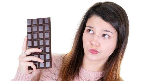 Jeune femme en bonne santé tenant du chocolat en pensant à gauche
