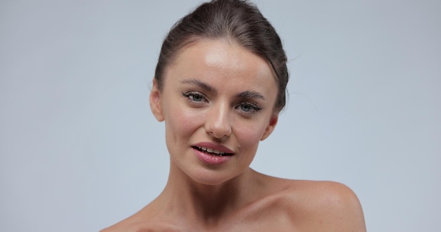 Jeune femme en bonne santé touchant une peau lisse sur le visage pour le concept de soins de beauté sur fond gris