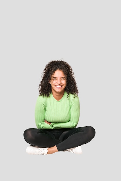 Jeune femme bouclée afro-américaine assise sur le sol isolée