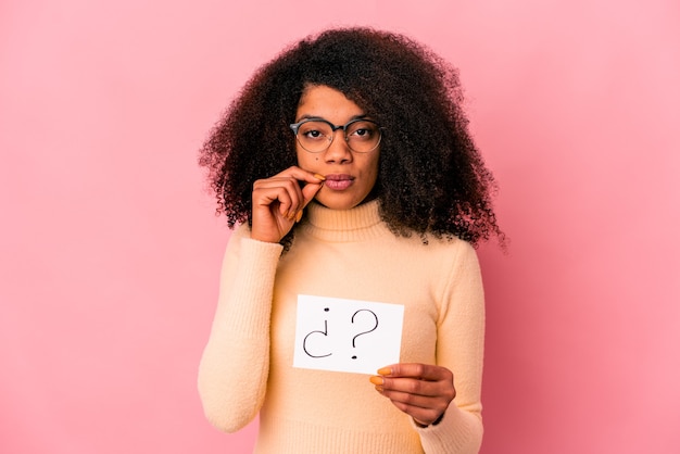 Jeune femme bouclée afro-américaine tenant un interrogatoire sur une pancarte avec les doigts sur les lèvres en gardant un secret.