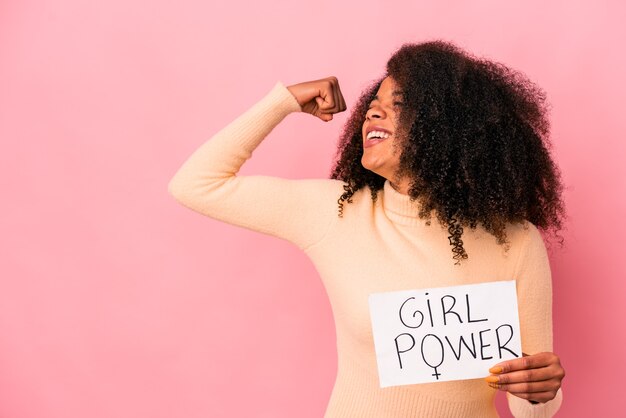 Jeune femme bouclée afro-américaine tenant un message de puissance de fille sur une pancarte levant le poing après une victoire, concept gagnant.