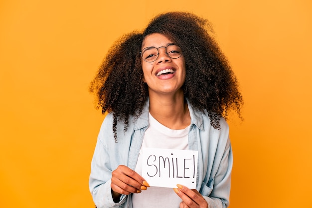 Jeune femme bouclée afro-américaine tenant une pancarte de message sourire en riant et en s'amusant.