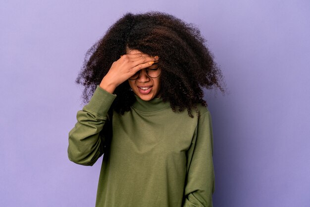 Jeune femme bouclée afro-américaine sur violet ayant mal à la tête, touchant l'avant du visage.