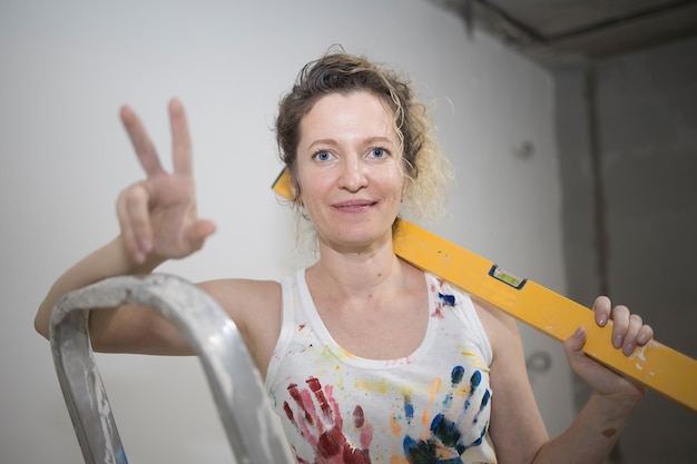 Photo jeune femme bouclée aux cheveux blonds fait des réparations dans le logement avec des outils de construction