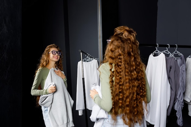 Photo jeune femme bouclée choisissant des vêtements au concept de shopping de cabine d'essayage