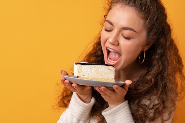 Jeune femme bouclée fit tenant un morceau de gâteau sur fond jaune