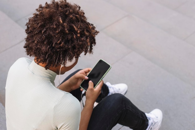 Jeune femme bouclée tapant un message texte via son smartphone Teen latine avec des boucles à l'aide de son téléphone portable