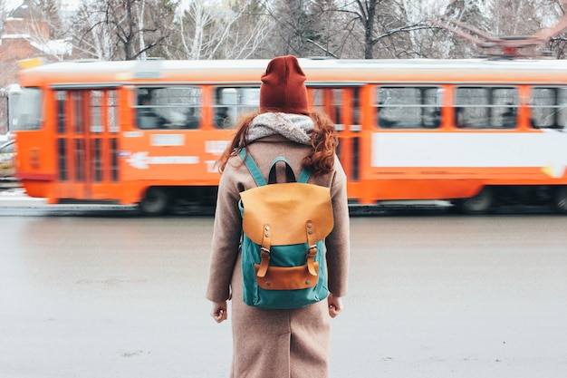 Jeune femme bouclée voyageuse tête rouge avec sac à dos devant le tramway dans la rue