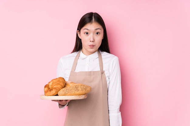 Jeune femme de boulanger chinois isolée hausse les épaules et les yeux ouverts confus.