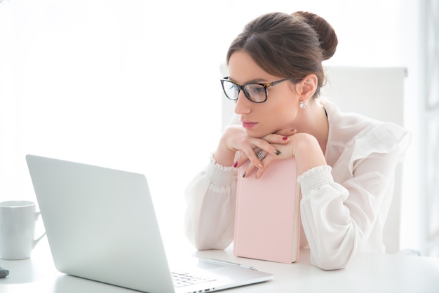 Une jeune femme bouleversée est assise dans un bureau devant un ordinateur portable et tient sa tête dans ses mains.