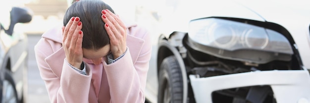 Une jeune femme bouleversée est assise avec la tête inclinée à côté d'accidents de voiture accidentés et de leurs conséquences