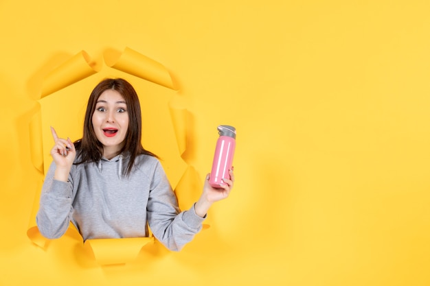 Jeune femme avec une bouteille d'eau sur fond de papier jaune athlète gym fit à l'intérieur