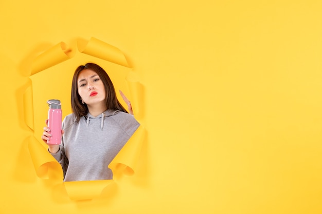 Jeune femme avec une bouteille d'eau sur fond de papier jaune déchiré athlète fit gym