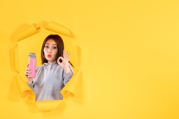 Jeune femme avec une bouteille d'eau sur fond de papier jaune déchiré gym fit athlète d'intérieur