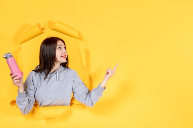 Jeune femme avec une bouteille rose sur une surface de papier jaune en forme d'athlète de gym en salle