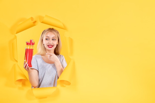 Jeune femme avec une bouteille rouge sur un mur jaune