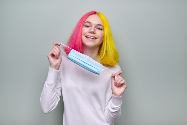 Jeune femme branchée à la mode en masque de protection médicale. Adolescente aux cheveux teints de couleur, sur fond pastel vert. Soins de santé et protection, épidémies, concept de jeunesse