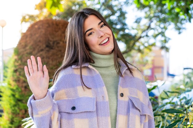 Jeune femme brésilienne dans un parc saluant avec la main avec une expression heureuse