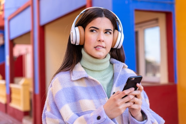 Jeune femme brésilienne à l'extérieur écoutant de la musique avec un mobile et pensant