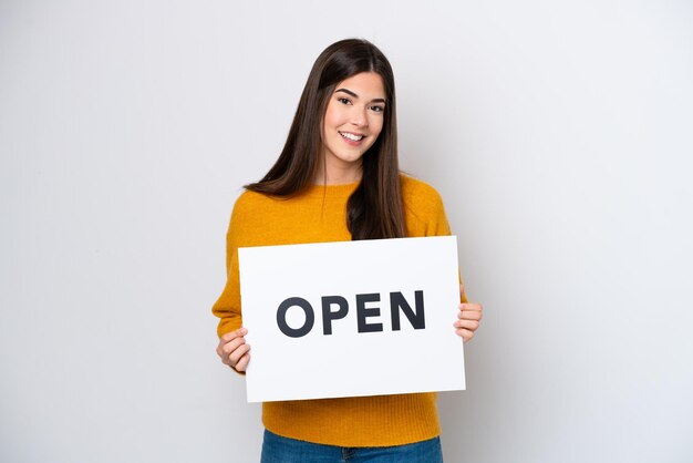 Jeune femme brésilienne isolée sur fond blanc tenant une pancarte avec texte OUVERT avec une expression heureuse