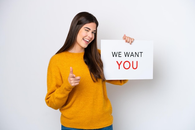 Jeune femme brésilienne isolée sur fond blanc tenant le tableau We Want You et pointant vers l'avant