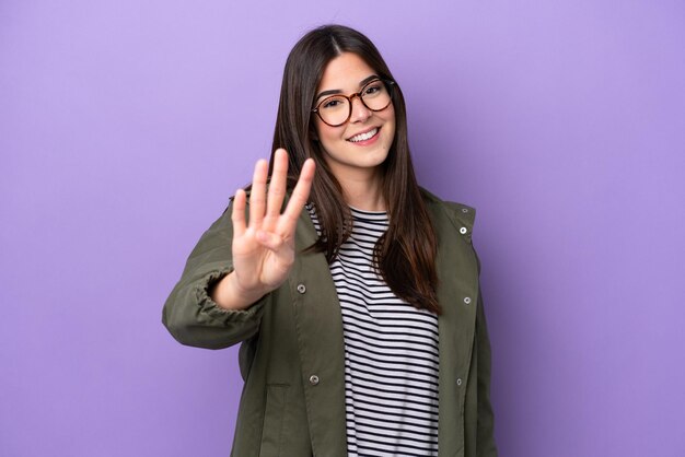 Jeune femme brésilienne isolée sur fond violet heureuse et comptant quatre avec les doigts