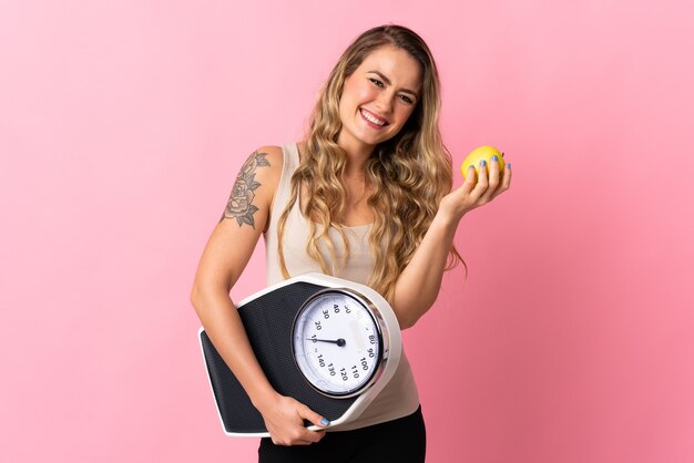 Jeune femme brésilienne isolée sur rose avec peseuse et avec une pomme