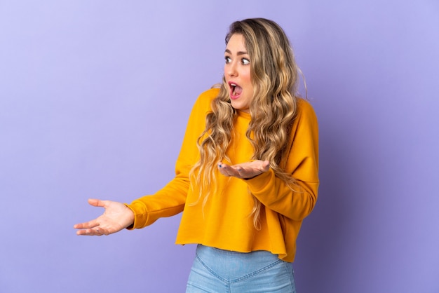 Jeune femme brésilienne isolée sur violet avec expression de surprise tout en regardant côté