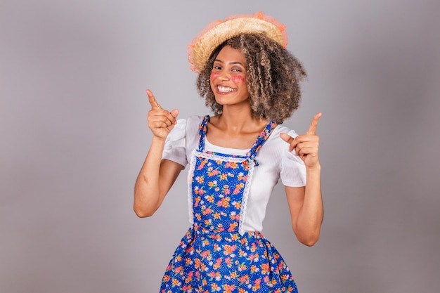 Jeune femme brésilienne noire avec des vêtements de pays habillés pour le festival Festa Junina Saint John optimiste et confiant pointant vers le ciel