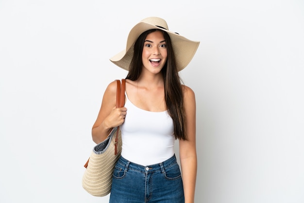 Jeune femme brésilienne avec Pamela tenant un sac de plage isolé sur fond blanc avec une expression faciale surprise