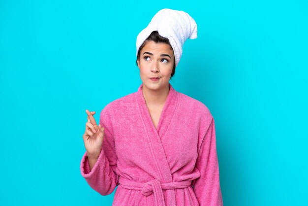 Photo jeune femme brésilienne avec un peignoir isolé sur fond bleu avec les doigts croisés et souhaitant le meilleur