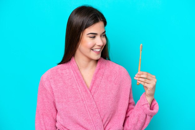 Jeune femme brésilienne se brosser les dents isolé sur fond bleu avec une expression heureuse