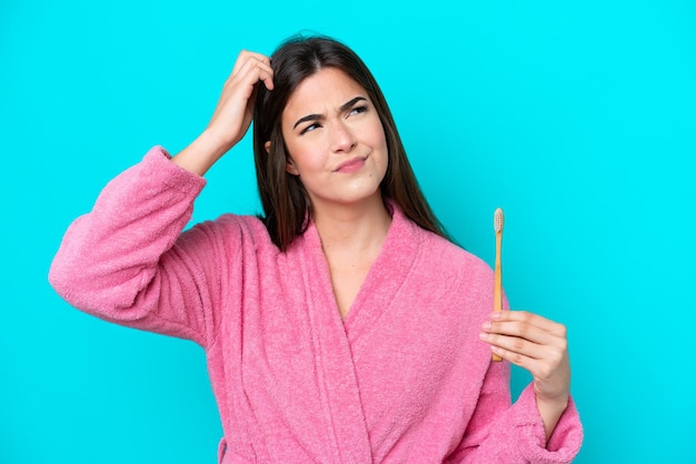 Jeune femme brésilienne se brosser les dents isolées sur fond bleu ayant des doutes et avec une expression de visage confuse