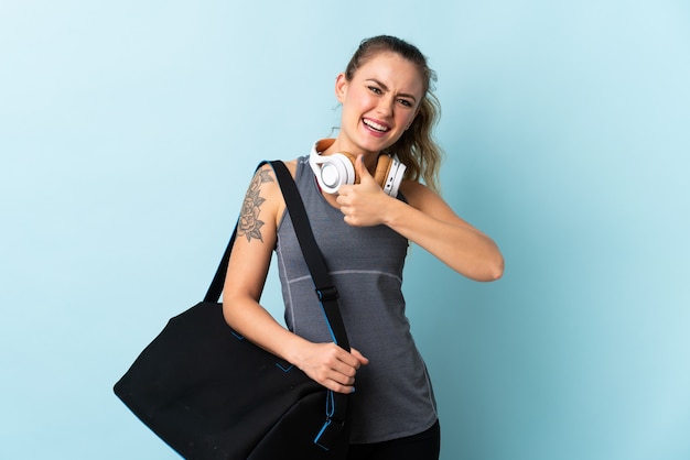 Jeune femme brésilienne de sport avec sac de sport isolé sur bleu donnant un geste de pouce en l'air