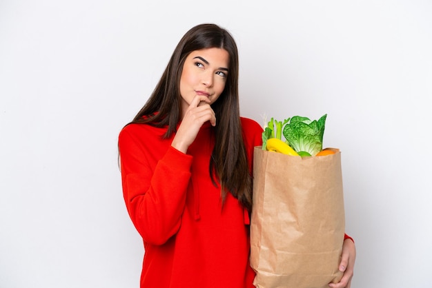 Jeune femme brésilienne tenant un sac d'épicerie isolé sur fond blanc et levant les yeux