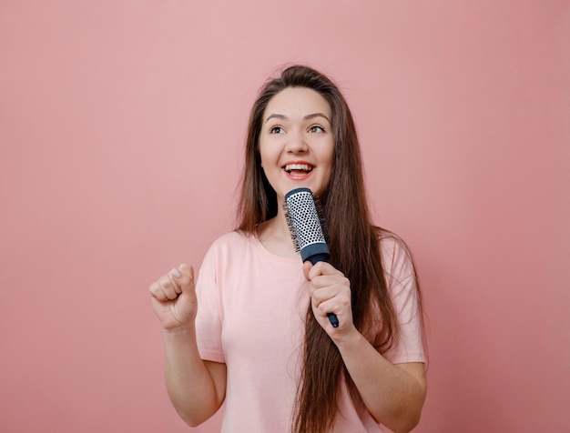 Jeune femme avec brosse à cheveux comme avec microphone à la main sur fond rose