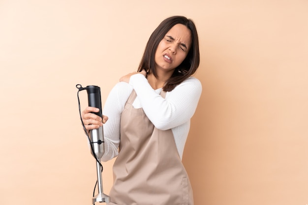 Jeune femme brune à l'aide d'un mixeur à main isolé