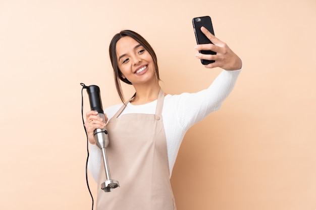 Jeune femme brune à l'aide d'un mixeur plongeant sur un mur isolé faisant un selfie