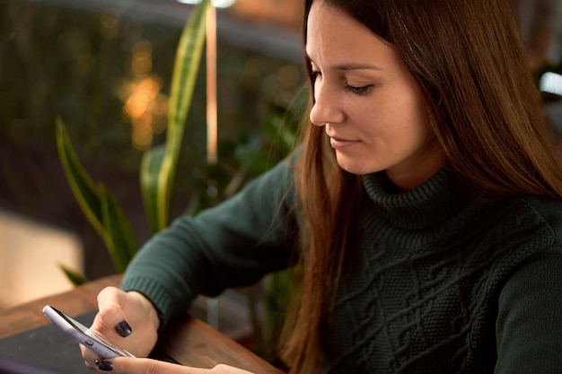 Jeune femme brune au café avec ordinateur portable communique par smartphone Close up