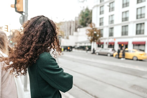 La jeune femme brune aux cheveux bouclés se tient sur l'arrêt de bus