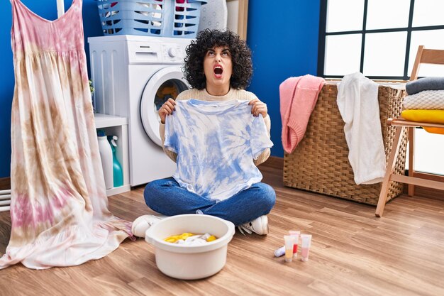 Photo jeune femme brune aux cheveux bouclés teinture tye die t-shirt et robe en colère et folle criant frustré et furieux, criant de colère en levant les yeux.