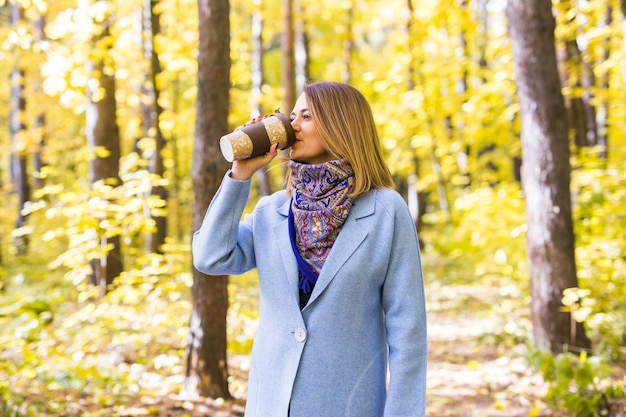 Jeune femme brune boit du café à l'automne parc