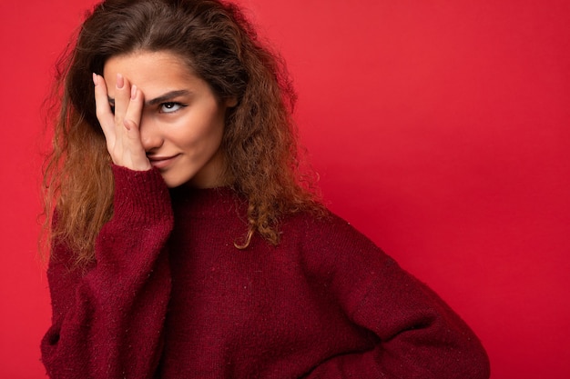 Jeune femme brune bouclée attrayante avec des émotions sincères en suspens isolées sur fond