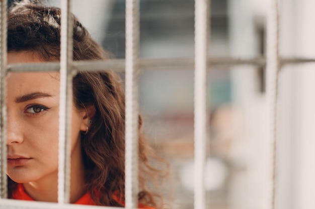 Jeune femme brune bouclée en costume orange derrière les barreaux de la prison