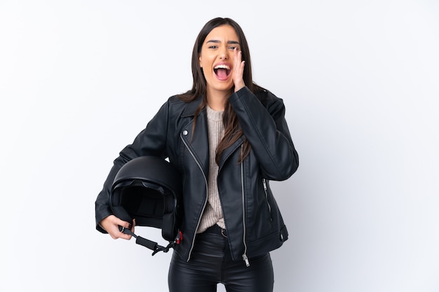 Jeune femme brune avec un casque de moto sur un mur blanc isolé criant avec la bouche grande ouverte