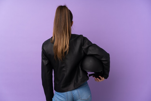 Jeune femme brune avec un casque de moto sur un mur violet isolé en position arrière