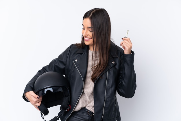 Jeune femme brune avec un casque de moto et tenant une clé sur un mur blanc isolé