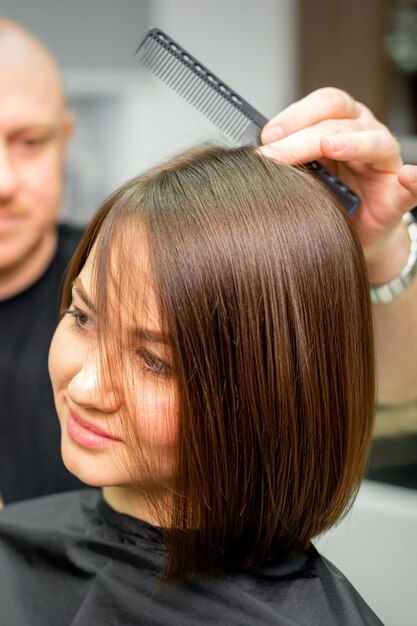 Jeune femme brune caucasienne ayant sa coiffure par un coiffeur masculin dans un salon.